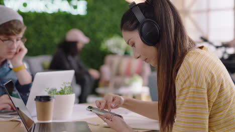 beautiful young asian woman student using laptop computer working on creative project browsing online research writing notes enjoying study listening to music wearing headphones in trendy office