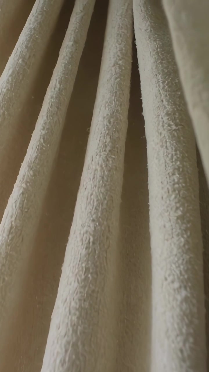 Vertical video: Panning camera down showing cream drape folds at room window centering dust specks