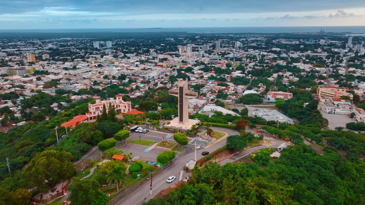 Allontanandosi dalla Croce del Guardiano, un punto di riferimento prominente a Ponce, Porto Rico. Vasto paesaggio urbano con molta vegetazione al tramonto, visto da drone.