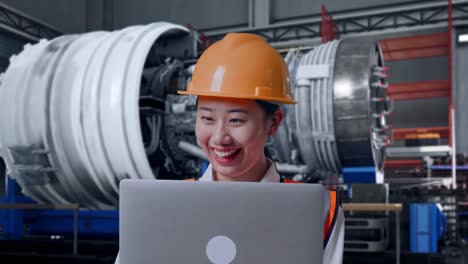close up of asian female engineer with safety helmet working on a laptop while standing with airplane engine maintenance conducted