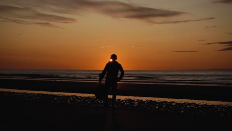 Man-running-with-guitar-in-back-sand-beach-at-sunset