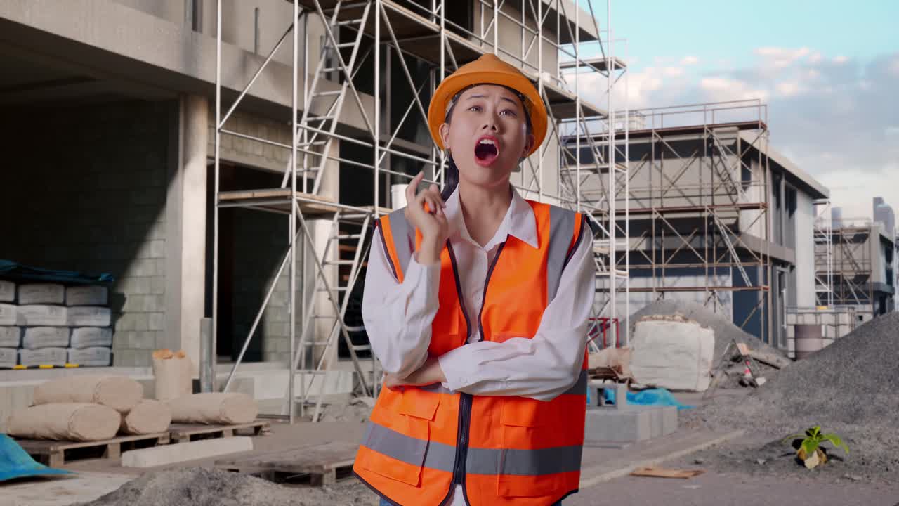 Asian Female Engineer With Safety Helmet Thinking And Looking Around Then Raising Her Index Finger While Standing At Construction Site in Progress to New House