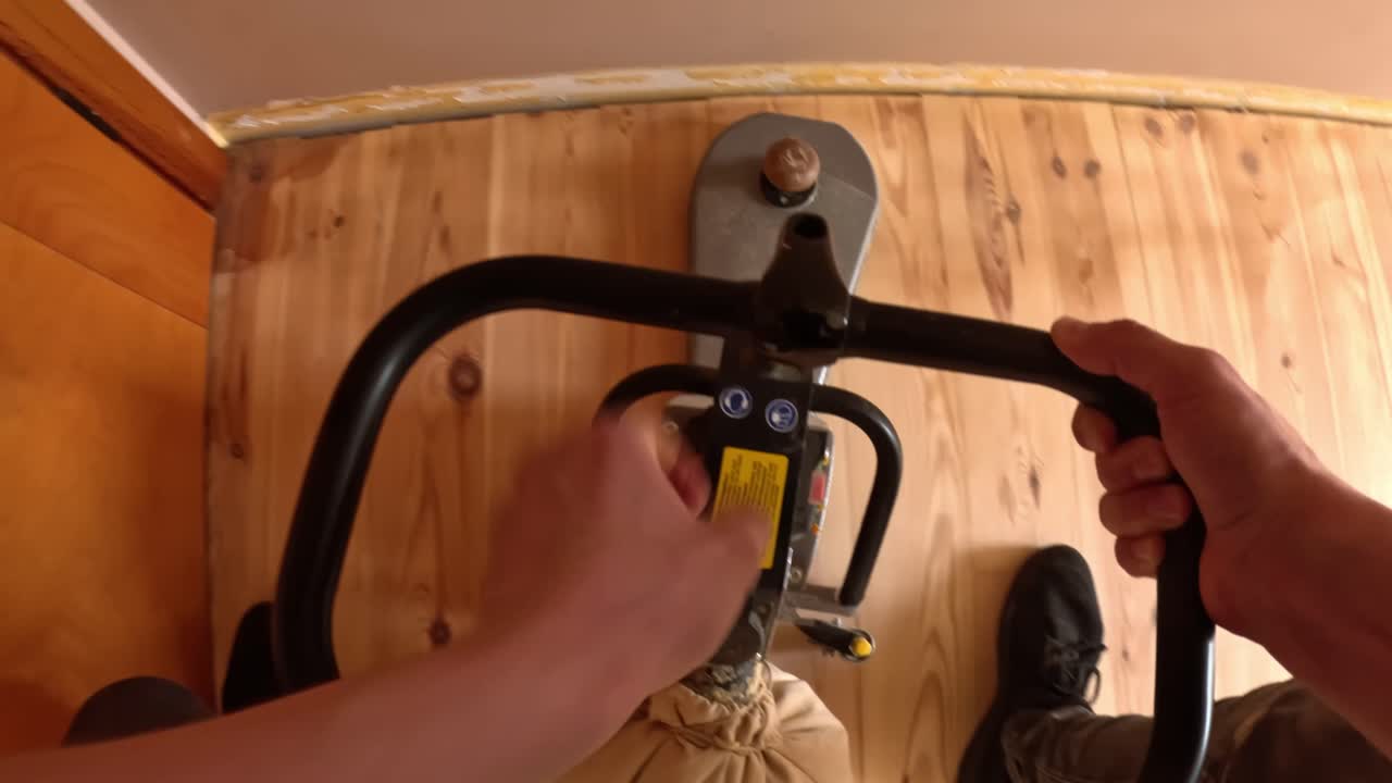 POV shot of a worker turning off a floor sander mid-project, showing hands on the handle as the machine powers down over freshly sanded wooden flooring