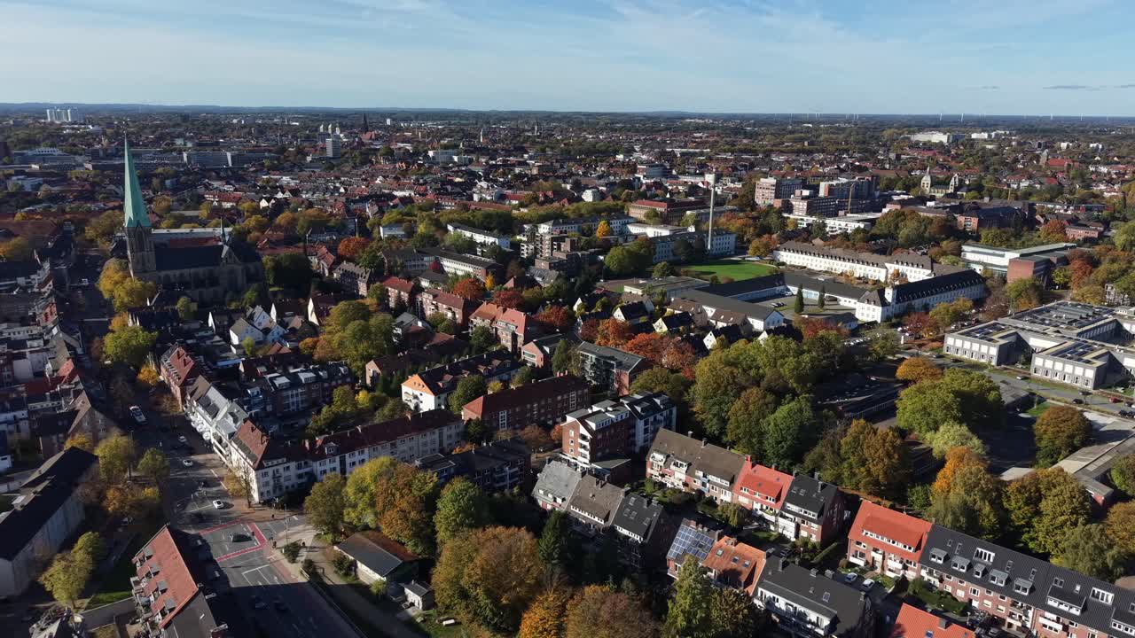 Aerial flyover shot of German neighborhood with colored trees at sunset. Church tower and historic row of homes with blue sky in fall. Wide shot. Peaceful city landscape of Münster