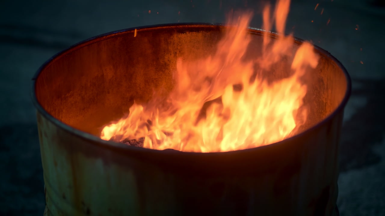 Barrel Fire Glowing In Urban Night, Rusty Metal Drum Burning With Steady Orange Flames, Smoky Asphalt Surface,