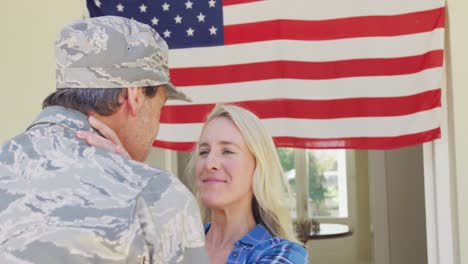 Kaukasischer-Männlicher-Soldat-Umarmt-Seine-Lächelnde-Frau-über-Der-Amerikanischen-Flagge