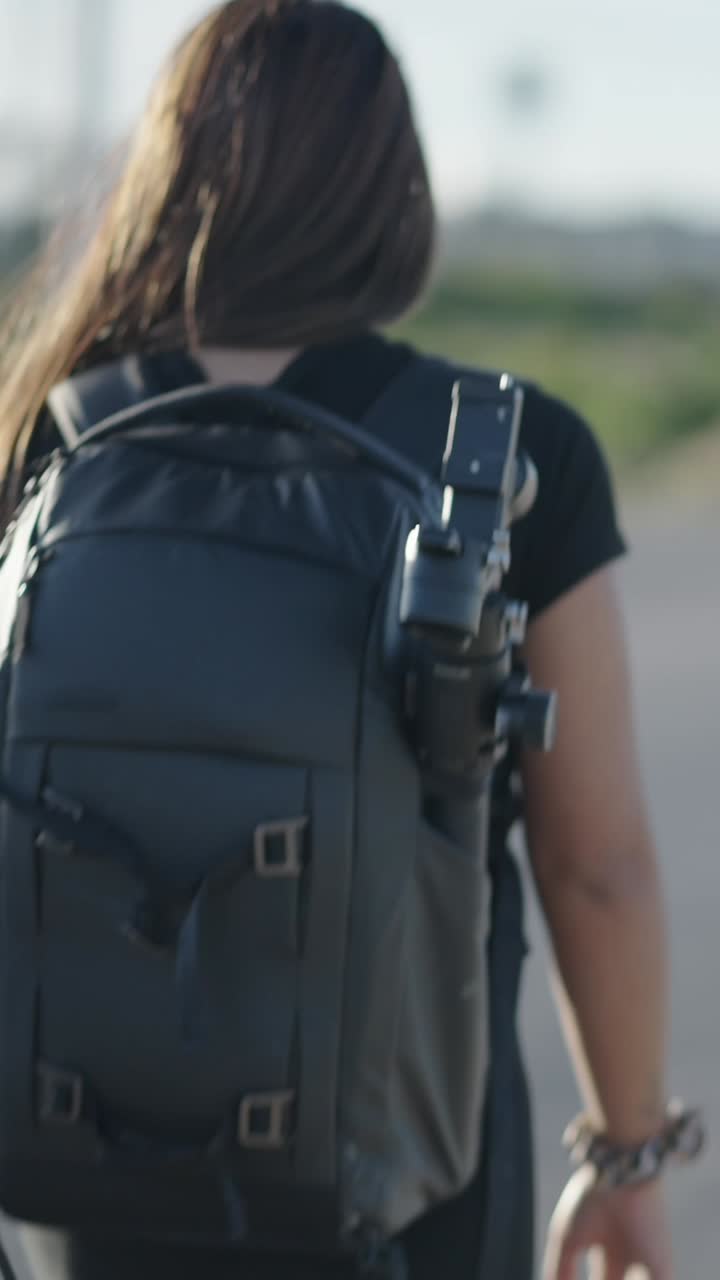 A woman walks along a street with a camera backpack