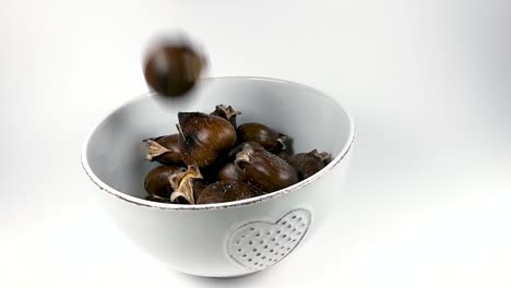 roasted chestnuts falling into white ceramic bowl, still, slomo, isolated