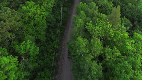 Drone-footage-of-car-with-canoe-driving-up-NH-White-Mountains-through-forest-on-dirt-road