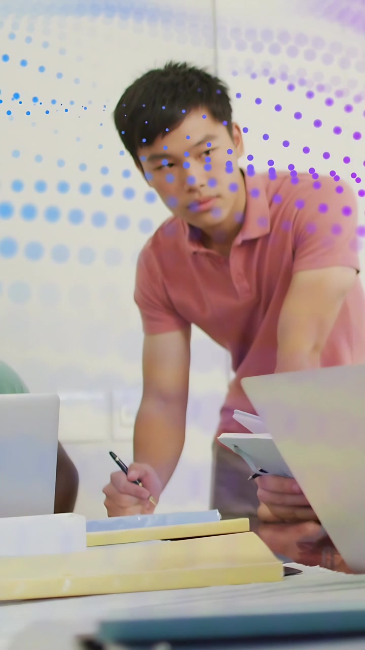 Video vertikal: Pria mencondongkan tubuh melihat rekan menunjukkan tablet, mencatat bisnis sementara titik-titik melapisi.