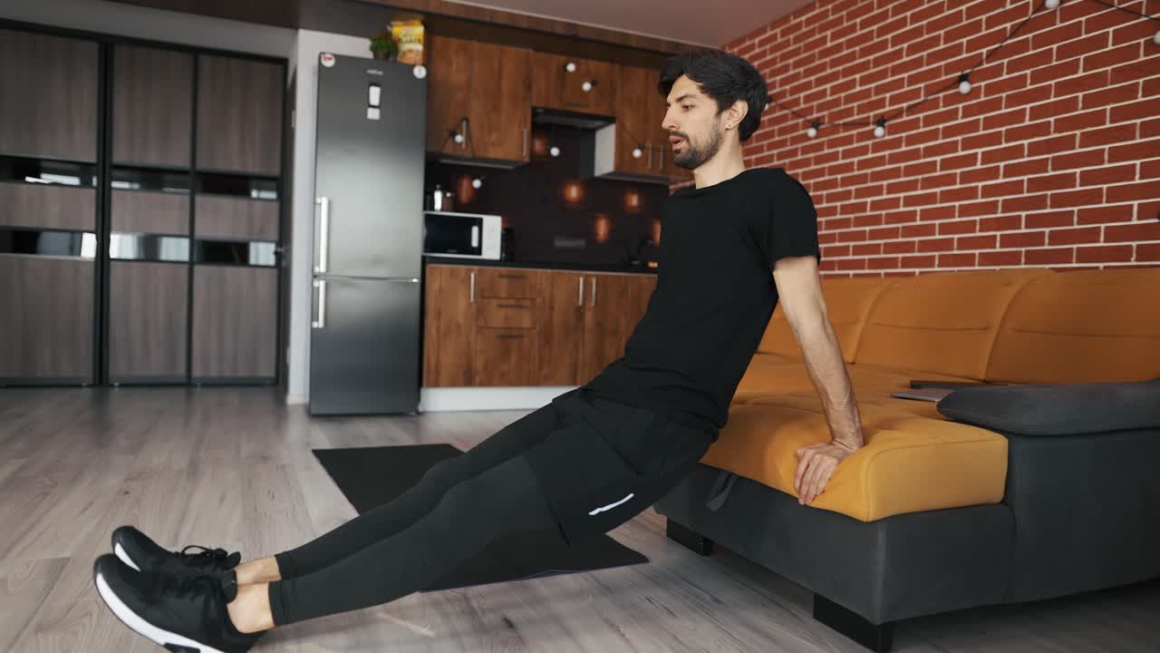 hombre atlético haciendo push up apoyado en el sofá en casa
