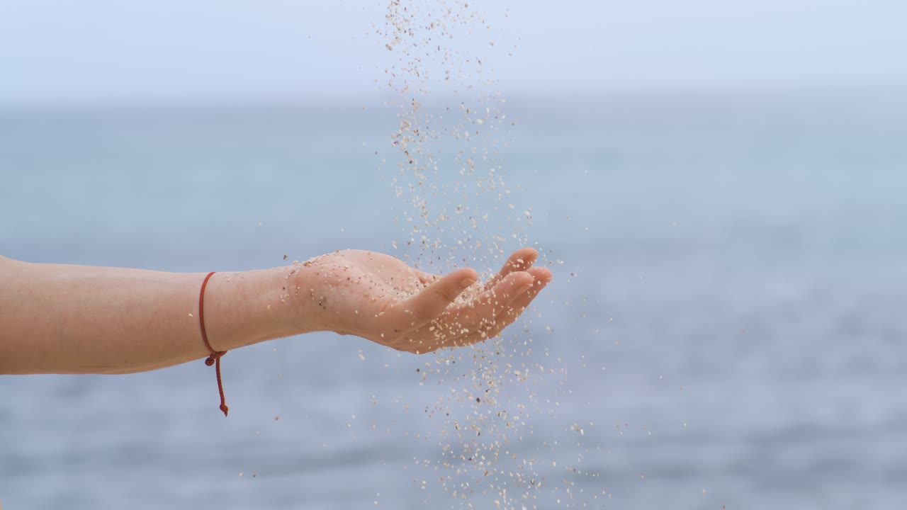 Sand falling from hand in slow motion on a beach. Vacation and travel concept. Shot on super slow motion camera 1000 fps
