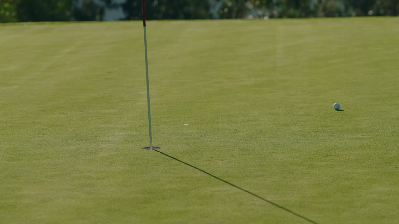 Golf ball moving near hole as golfer stands on green