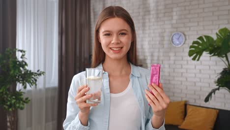 Young Woman Preparing a Refreshing Drink by Pouring Powder Collagen into a Glass a Young Woman Pours Powder Collagen into a Glass of Water Smiling and Preparing a Refreshing Drink in a Modern Kitchen Healthy Living Concept Taking Vitamins for Skin and Hair Beauty