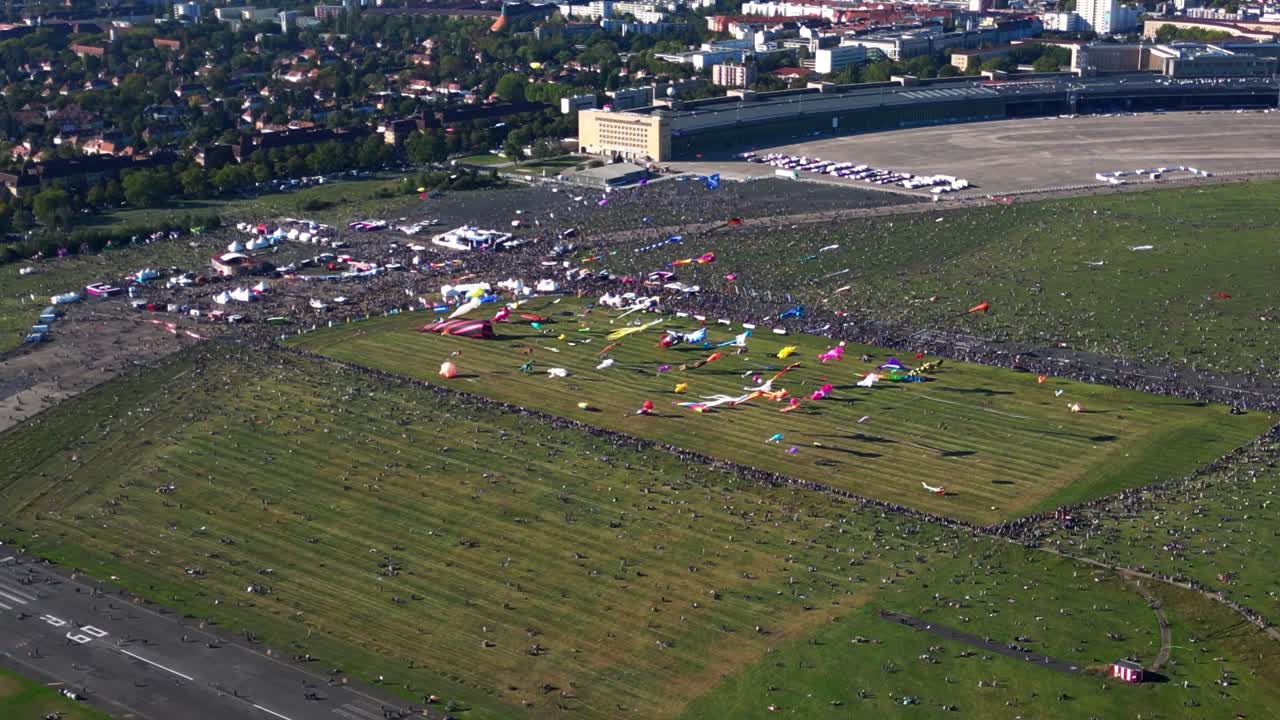 Large crowd of people gathering at the Tempelhofer Feld giant kite festival in Berlin, Germany. Gorgeous aerial view flight fly reverse drone