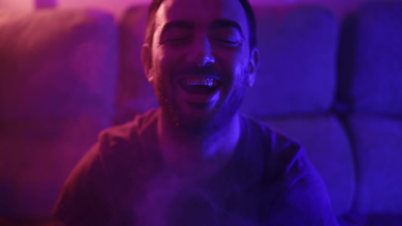 Uomo che ride malvagiamente con fumo illuminato di rosso e blu che lo circonda.