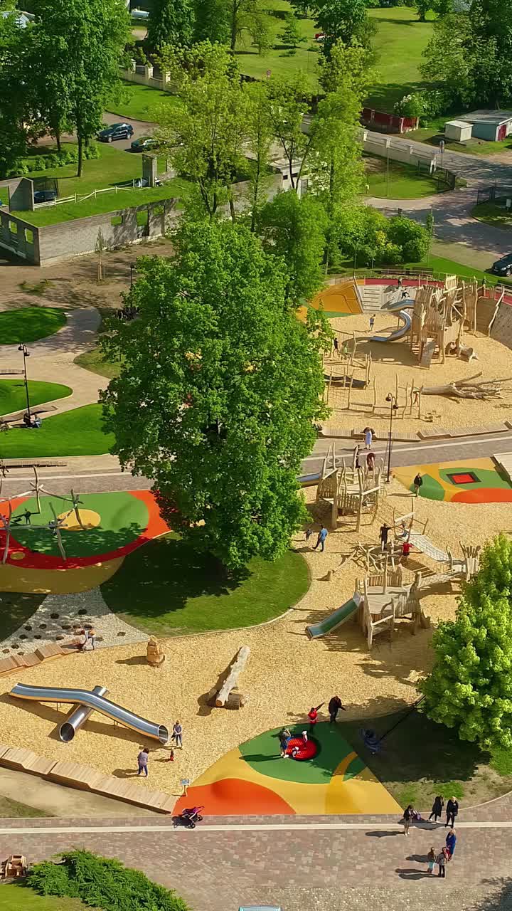Children playing and having fun at a large, modern, and colorful public playground with slides and sand pits on a sunny summer day in Latvia - An aerial vertical parallax shot