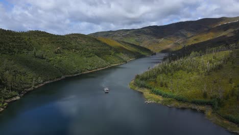 aerial view of an amazing solar boat travelling along pinewood forest valleys on a cloudy day