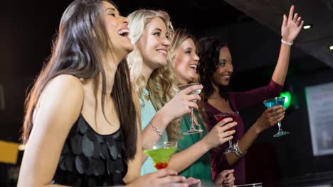 happy diverse female friends laughing and holding cocktail drinks at bar