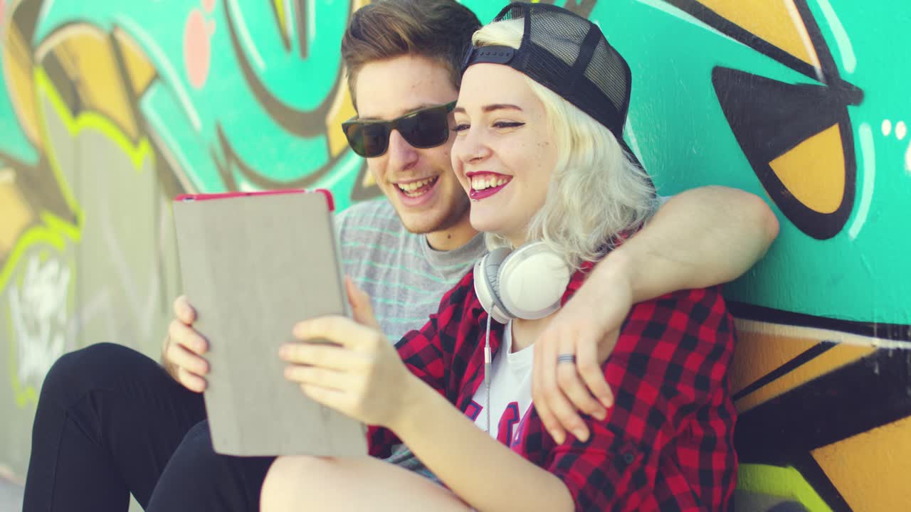 pareja joven hipster riendo revisando una tableta