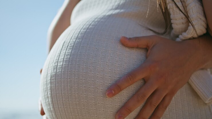 Primo piano della pancia di una donna incinta alla luce del sole. Mani del marito che accarezzano la pancia.