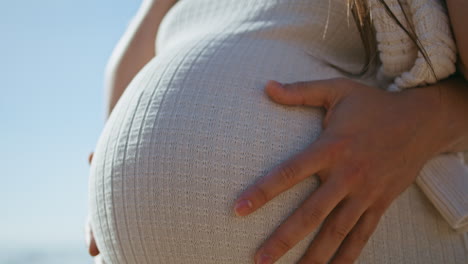 closeup pregnant female belly at sunlight. unknown husband hands caressing tummy