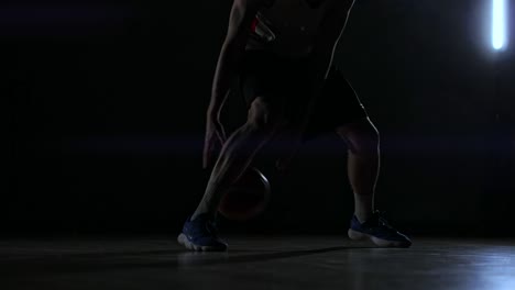 어두운 농구장에서 농구 링을 배경으로 농구 공을 들고 있는 한 남자가  ⁇ 빛에 세 개의 등불로 조명된 드리블링 기술을 보여줍니다.