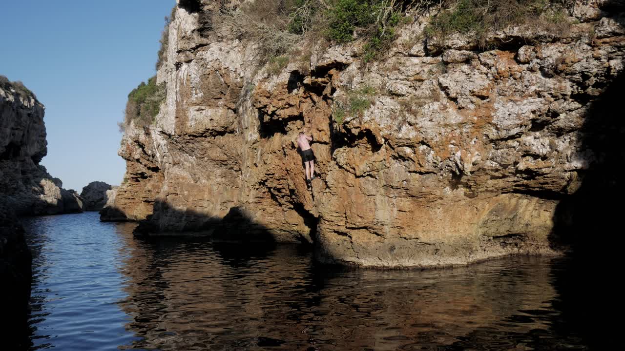 Climber performing deep water soloing at Cala Rafaelet, sea cliff, no ropes