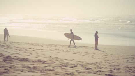 surfista sosteniendo una tabla de surf y alejándose del agua del océano y las olas en el soleado atardecer