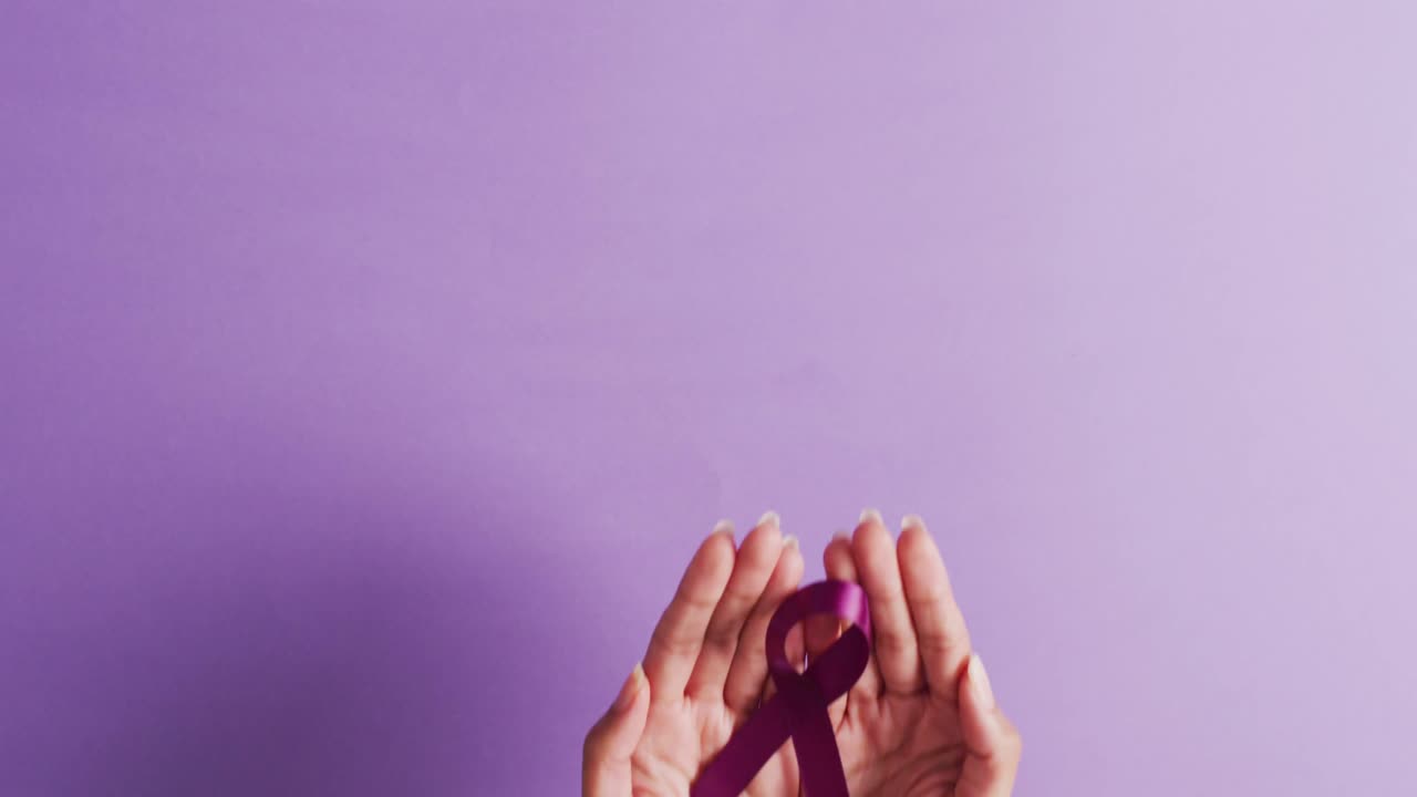 Video delle mani di una donna caucasica che tengono un nastro viola su sfondo viola.