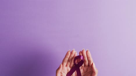 Video-of-hands-of-caucasian-woman-holding-purple-ribbon-on-violet-background