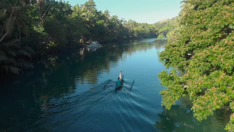 Un-Dron-Aéreo-Mágico-Al-Atardecer-Disparado-Desde-Un-Barco-Local-Con-Gente-En-Un-Gran-Río-A-Través-Del-Verde-Y-Exuberante-Bosque-Selvático-Con-Palmeras