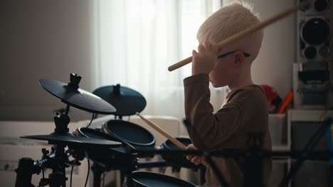 Un-Pequeño-Niño-Albino-Con-Cabello-Blanco-Y-Gafas-Redondas-Azules-Toca-Una-Batería-Electrónica-En-Su-Habitación.-Un-Niño-Feliz-Con-Talento-Para-Tocar-Instrumentos-Musicales-Sostiene-Baquetas-En-Sus-Manos-Y-Toca-La-Batería.