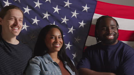 studio portrait shot of multi-cultural group of friends holding american flag behind them celebrating 4th july independence day 3