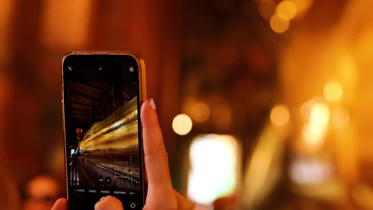 A person photographs a golden statue using a smartphone in a warmly lit environment.