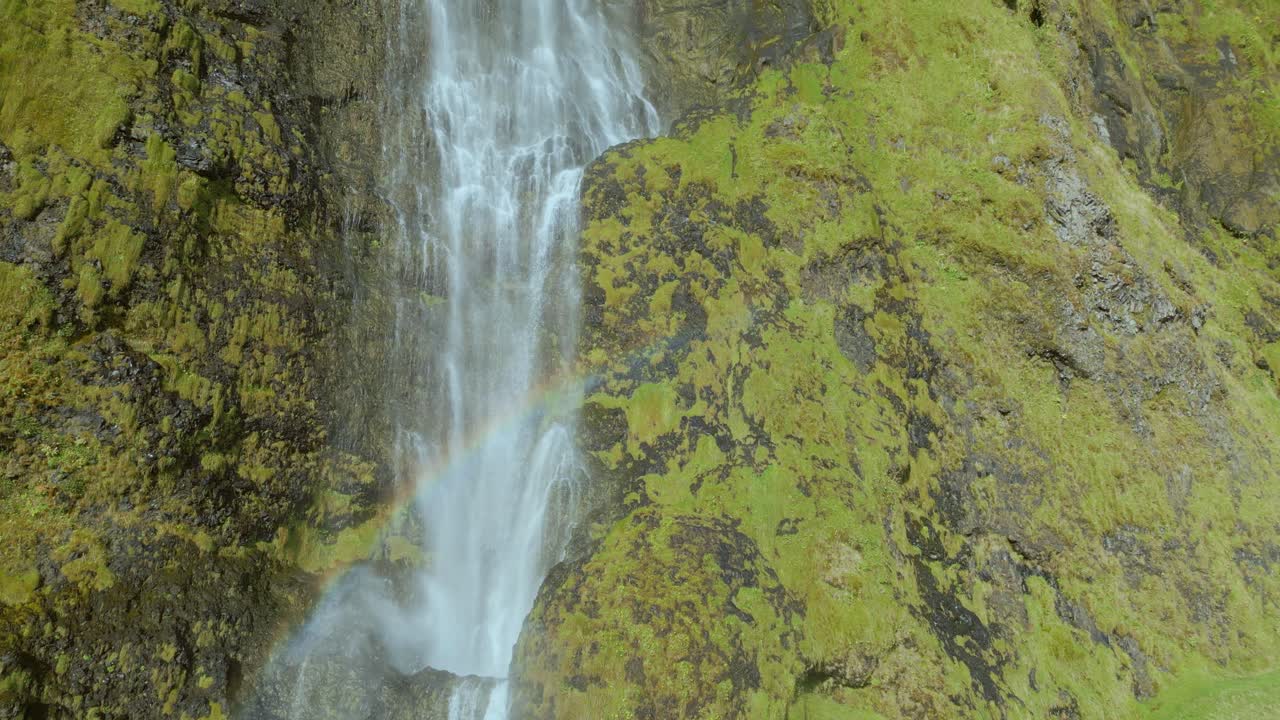 drone pan encima de una cascada que cae sobre grandes acantilados de musgo amarillo