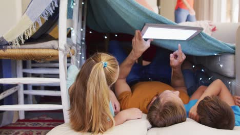 Caucasian-father,-son-and-daughter-lying-in-house-of-blankets-using-tablet-copy-space-on-screen