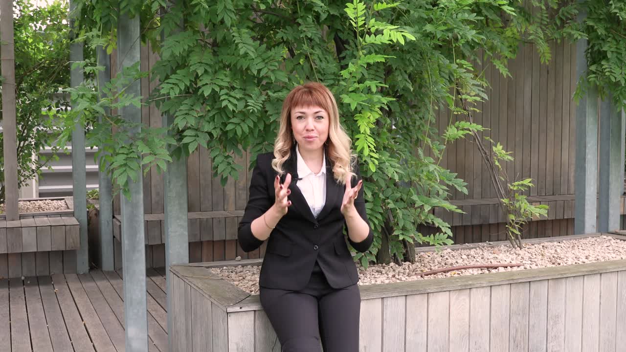 비즈니스 슈트를 입은 긴 금발 머리카락을 가진 아름다운 소녀는 인터뷰를합니다. 블로거. 기자. 뉴스. 젊은 사업가 여성은 언론인에게 자신의 회사에 대한 인터뷰를 제공합니다. 거리의 공원에서 인터뷰