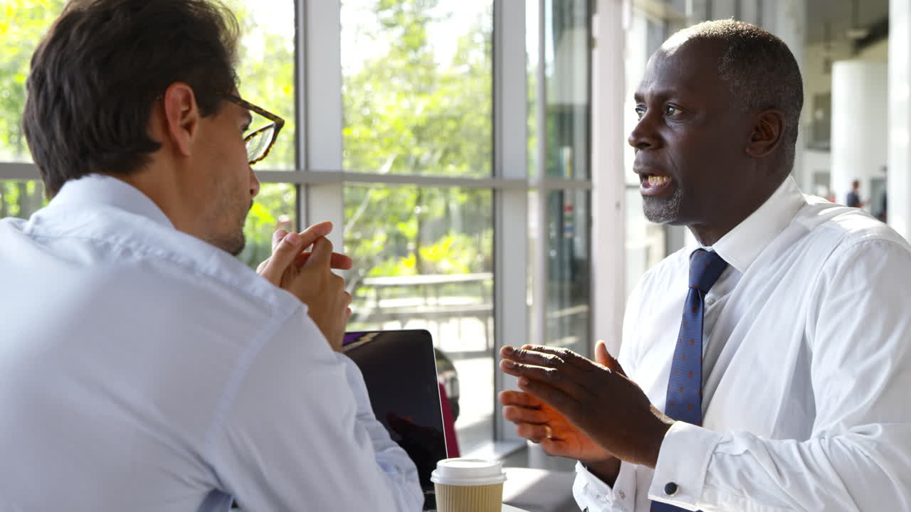 Two Businessmen Having Meeting Around Table In Modern Office