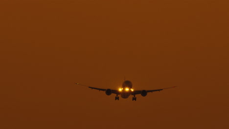 vista frontal - un avión con los faros encendidos llega a aterrizar en un aeropuerto y aterriza en una pista de aterrizaje al atardecer con un cielo de color naranja