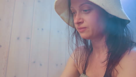woman wearing sauna hat sits wrapped in towel in misty room, taking care of herself in peaceful moment of relaxation, warm light glows softly through steam