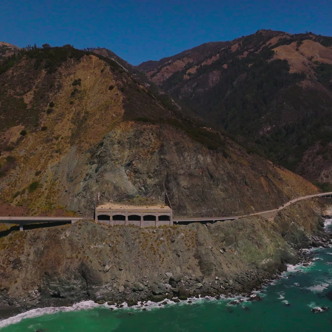 Road connecting the mountains at the coastline of California. Beautiful sight of the rugged rocks at the backdrop of blue clear sky