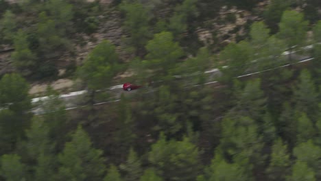 coche rojo a toda velocidad en la carretera de curvatura que pasa por árboles densos cerca de barcelona, españa