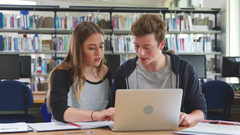 male and female college students working on laptop in library