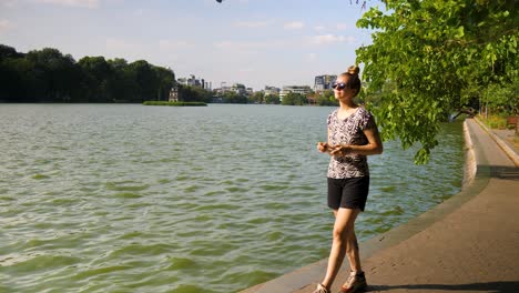 Young-tourist-stands-at-the-edge-of-Hoan-Kiem-lake,-Vietnam-to-capture-the-scene