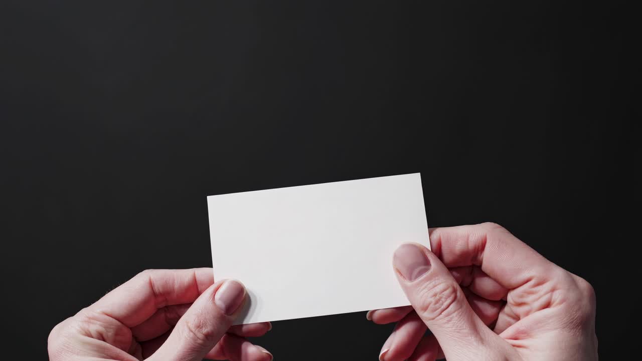 Close-up shot of hands holding a blank card against a dark background, ideal for a minimalist video