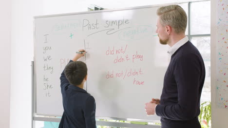 Männlicher-Grundschüler,-Der-Englische-Pronomen-Auf-Die-Tafel-Schreibt,-Während-Der-Lehrer-Ihn-Ansieht-1