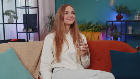 Thirsty-one-young-woman-sitting-at-home-holding-glass-of-natural-aqua-make-sips-drinking-still-water