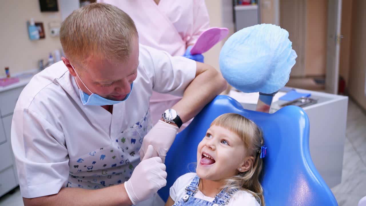 Happy little child in dental chair. Man dentist talks to a little girl before treating her teeth. Smiling child at stomatologist office.