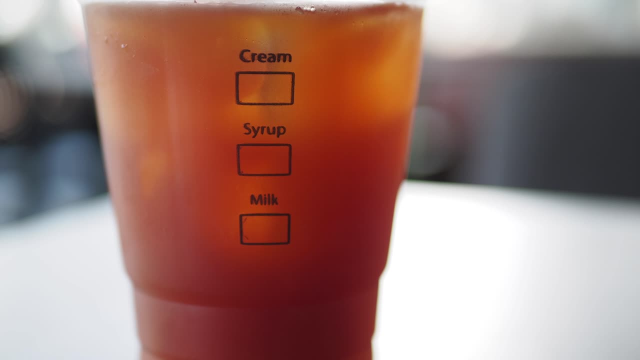 primer plano de una taza de café helado con crema, jarabe y opciones de leche